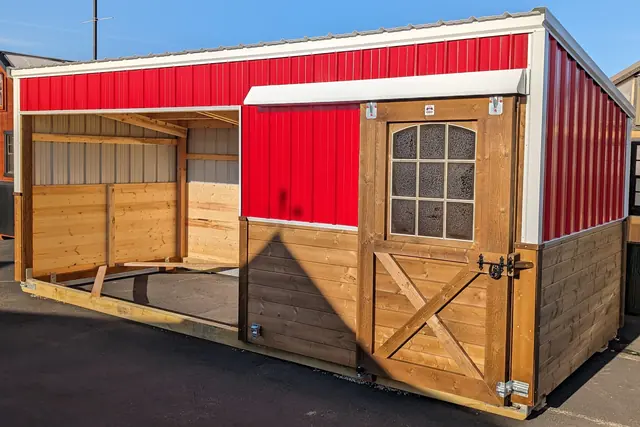 Small shelter with red metal upper walls, an open bay on one side and a windowed door with a cross-braced lower panel, on blacktop