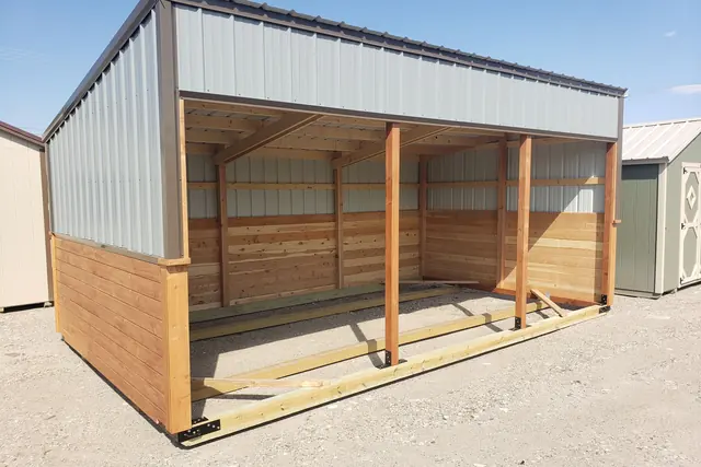Open-front run-in shelter with gray metal upper walls, wood lower walls and posts across the front, on a gravel lot