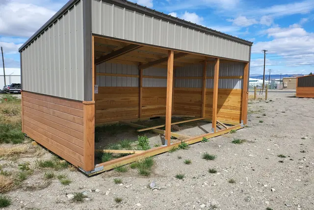 Open-front run-in shelter with tan metal upper walls, wood lower walls and posts across the front, on a gravel lot