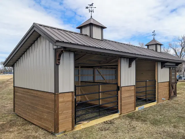 Horse stable with brown roof, two cupolas with weathervanes, gated stalls and stained wood lower walls