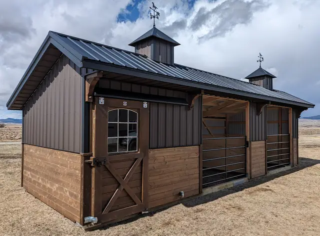 Horse stable with an arched-window Dutch door, dark siding, two cupolas and open gated stalls