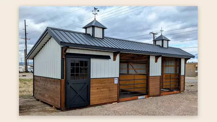 12×32 deluxe horse stable in Helena: two gated stalls and a black tack room door under a black metal roof with two cupolas